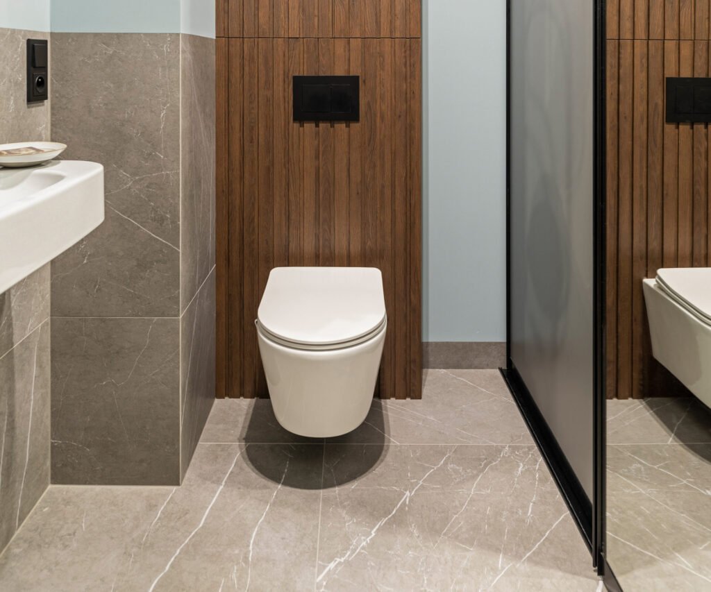 modern bright bathroom with white toilet seat wooden lamela wall mirror grey wall scaled e1776533085973